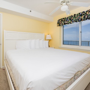 This bright bedroom features a king bed with plush pillows and a stunning beachfront view through large windows