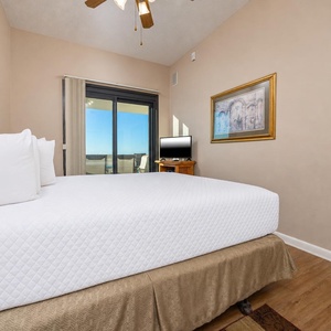 Bright and airy master bedroom featuring a king bed, a TV, and access to the balcony with a view of the beach