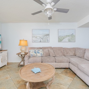 Relax on the sectional sofa while enjoying the coastal decor, large TV, and beachfront balcony views