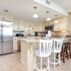 The well-equipped kitchen features light cabinetry, granite countertops, and a breakfast bar with two stools