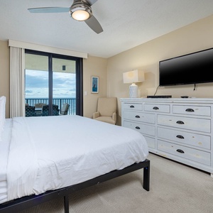 A cozy master bedroom features a king bed, a wall-mounted TV, and a private balcony with a view of the beach front
