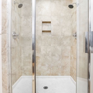The master bath features a sleek walk-in glass shower with elegant tile work, offering a refreshing retreat after a beach day