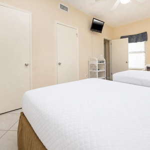 Guest room featuring two double beds, a wall-mounted TV, and cheerful decor with natural light streaming through the window