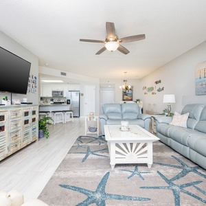 Cozy living area features a light blue sofa, a rustic media console, coastal decor, and a view into the inviting kitchen