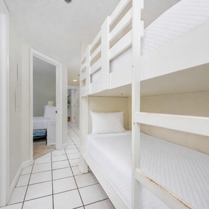 This cozy bunk area features white wooden beds and a welcoming view towards the nearby guest bedroom