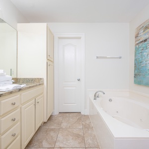 Bright and inviting master bathroom featuring a jetted tub, elegant granite countertops, and soothing coastal artwork