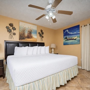 A spacious bedroom features a king bed with plush white bedding, decorative artwork, and a TV for entertainment
