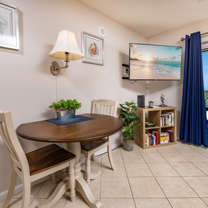 The living area features a cozy dining table, a wall-mounted TV, and stunning beach views through balcony doors
