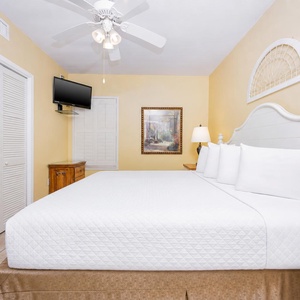 Spacious bedroom features a king bed, wall-mounted TV, and warm yellow walls, creating a relaxing retreat for guests