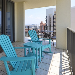 Turquoise rocking chairs and a small table create a relaxing balcony space with views of the surrounding area