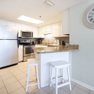 Bright kitchen featuring white cabinetry, granite countertops, and a breakfast bar with two stools for casual dining