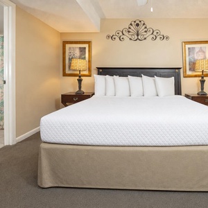 The bedroom features a king bed with decorative pillows, bedside lamps, and a bathroom entry with a floral shower curtain