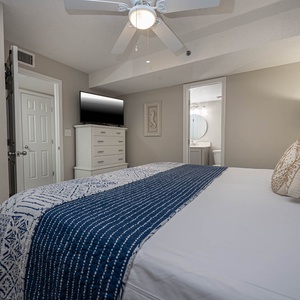 This cozy bedroom features a stylish decor, a flat-screen TV, and an en-suite bathroom with a round mirror
