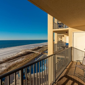 The balcony offers a serene view of the beach and pool area, complemented by two chairs for relaxing in the sun