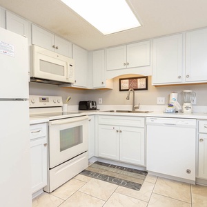 Bright white cabinetry and a cheerful beach-themed mat enhance this kitchen with white appliances and ample counter space