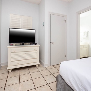 Bright guest room featuring a TV on a white dresser and an adjoining bathroom, offering a cozy retreat for relaxation
