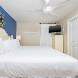 Bright bedroom featuring a king bed, a blue accent wall, a mounted TV, and a cozy ambiance enhanced by natural light
