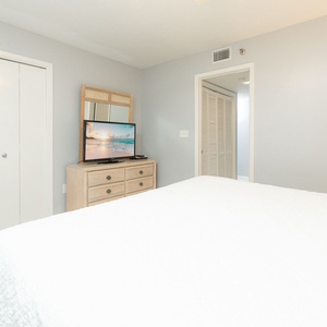 Bright guest bedroom featuring a plush king bed, a TV on a shelf, and natural light streaming through the window