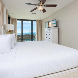 Spacious bedroom featuring a comfortable king bed, a TV, and large windows with a view of the beach