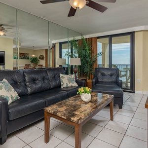 The living area features a leather sofa with queen sleeper, chair, and coffee table, showcasing a beach front view