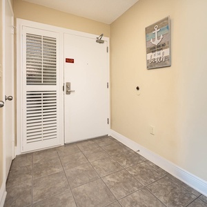 Welcoming entryway featuring tiled flooring, a decorative beach-themed wall art, and a secure door with a glass panel