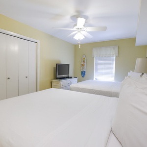This guest bedroom features two queen beds, a TV, and a cheerful yellow wall, creating a bright and welcoming atmosphere