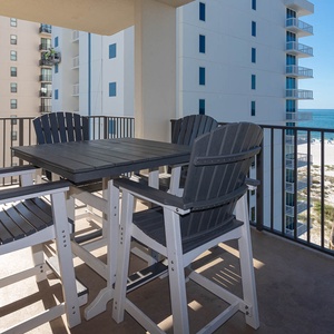 Stylish outdoor seating on the balcony offers a view of the beach and turquoise waters, perfect for enjoying the breeze
