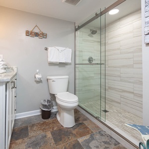 This bathroom features elegant stone flooring, a glass shower, and a beach-themed decor for a refreshing retreat