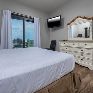 Bright master bedroom featuring a king bed, a TV, and a balcony view of the beach, complemented by elegant furnishings