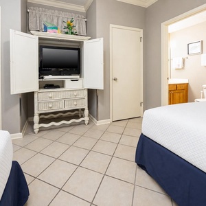 Guest room featuring two double beds, a TV on a decorative stand, and a doorway leading to a bathroom area