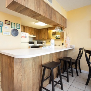 This kitchen features wood cabinetry, a spacious countertop, and a cozy bar area with seating, perfect for casual dining