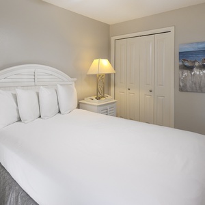 Cozy guest bedroom featuring a queen bed with plush pillows, a bedside lamp, and a coastal painting on the wall