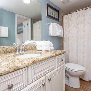 The bathroom features a granite countertop, elegant shower curtain, and neatly arranged towels for a refreshing experience