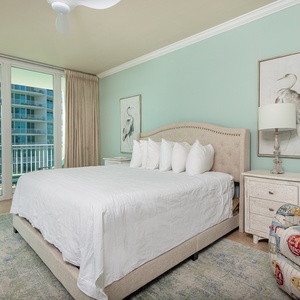 The master bedroom features a plush king bed, colorful accent chair, and large windows offering a bright view of the bay