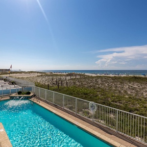 Enjoy a refreshing poolside view overlooking sandy dunes and vibrant beach umbrellas under a clear blue sky