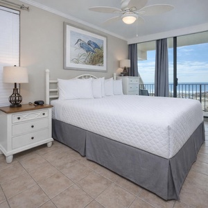 This bedroom features a king-sized bed, coastal decor, and a stunning beachfront view from the large sliding glass doors