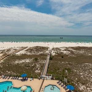 Expansive view of the beach with white sand, beach umbrellas, and the pool area below, inviting relaxation and fun