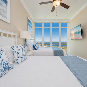 Guest suite with two queen beds welcomes you to rest while coastal scenery stretches beyond tall windows