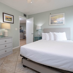 This serene guest bedroom features soft green walls, a queen bed with plush pillows, and charming decor for a relaxing stay