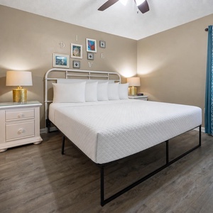 Brightly decorated bedroom featuring a large king bed, bedside tables with lamps, and framed art on the wall