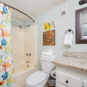 This bathroom features a colorful fish-themed shower curtain, a granite countertop, and fresh towels for a refreshing stay