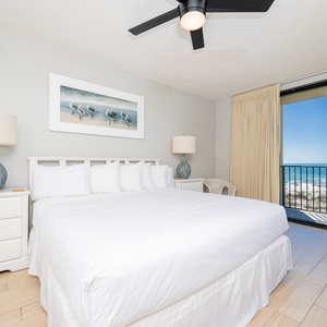 Relax in the inviting master bedroom featuring a king bed, coastal artwork, and stunning balcony views