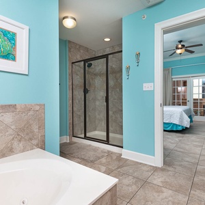 The master bath features a relaxing jetted tub, a walk-in shower, and vibrant aqua walls, leading to a cozy bedroom beyond