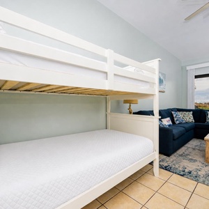 Cozy living space features a twin bunk bed with fresh linens and a sofa adorned with colorful pillows, plus a beach view