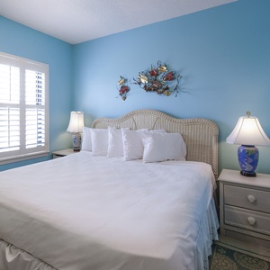 Cozy guest bedroom featuring a plush king bed, soft white linens, and vibrant blue walls accented by decorative fish art