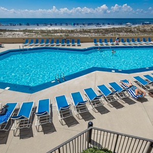 The pool area surrounded by lounge chairs with a view of the beach and umbrellas in the distance