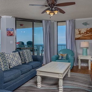 Living area features a blue sofa with queen sleeper, a turquoise chair, and a stunning view of the beach from the balcony