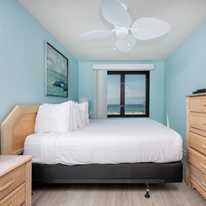 The master bedroom features a plush bed, a TV, and a stunning beachfront view through the large window