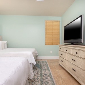 This inviting guest bedroom features two comfortable beds, a large TV, and soft green walls, creating a restful retreat