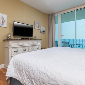 The master bedroom features a large bed, a TV, and a stunning beachfront view from the balcony